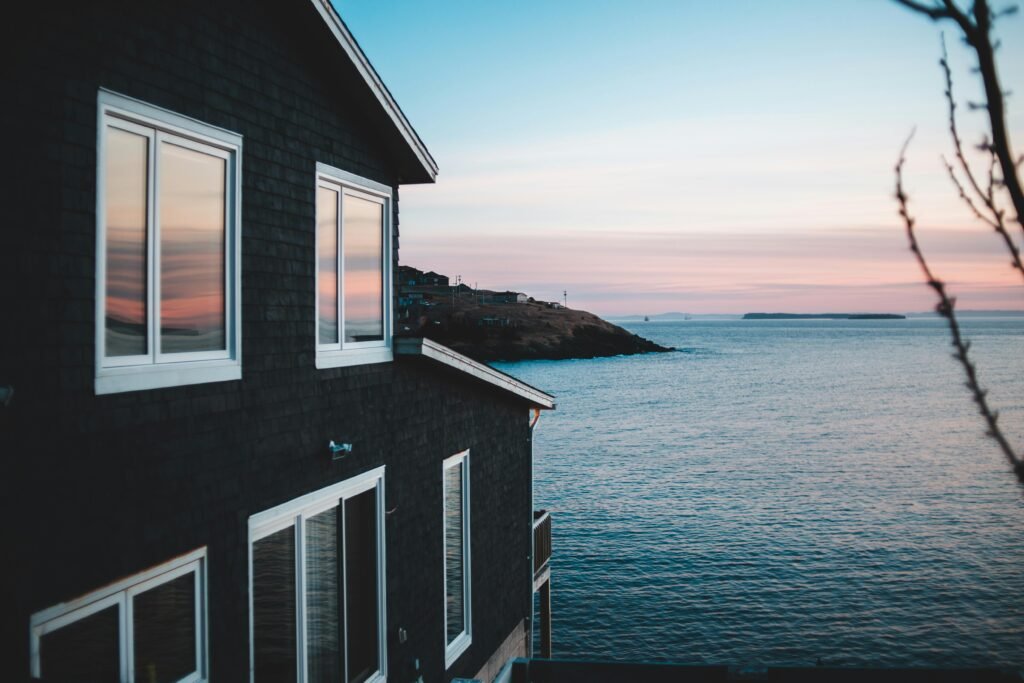 A serene view of a coastal house with the ocean at sunset, capturing tranquility and natural beauty.
